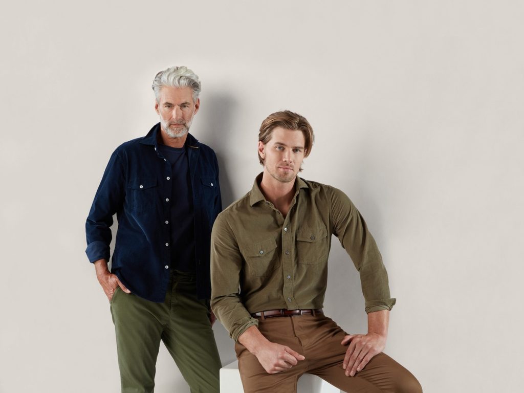 A sitting young male model and a standing older male model in formal dresses