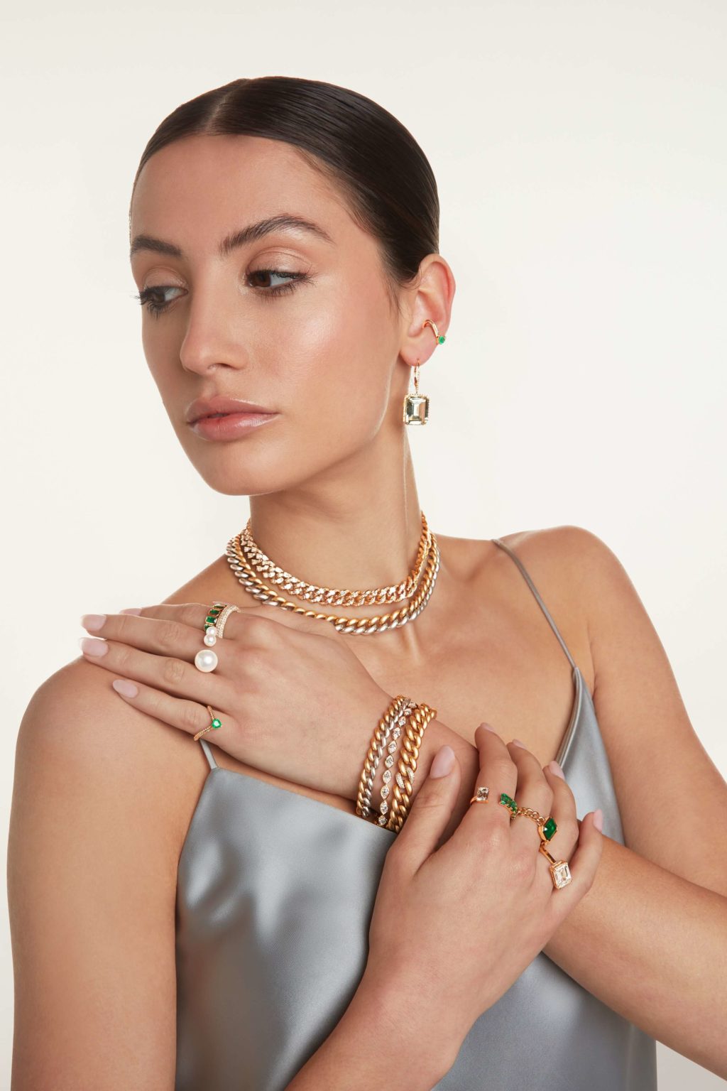 A model girl touching her shoulder with her hand having visible rings , bracelet and necklace
