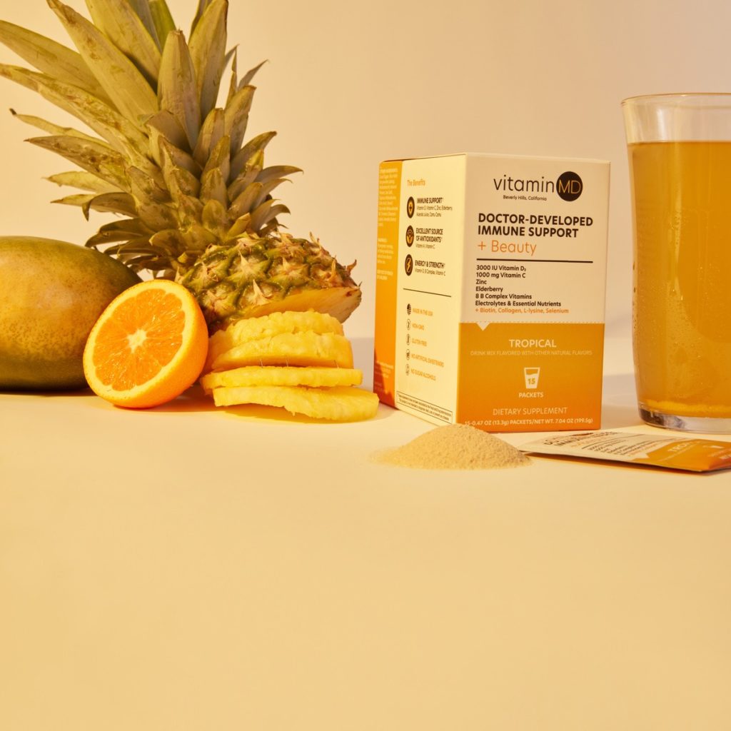 Image of a Vitamin MD powder pack along with sliced pineapple and orange