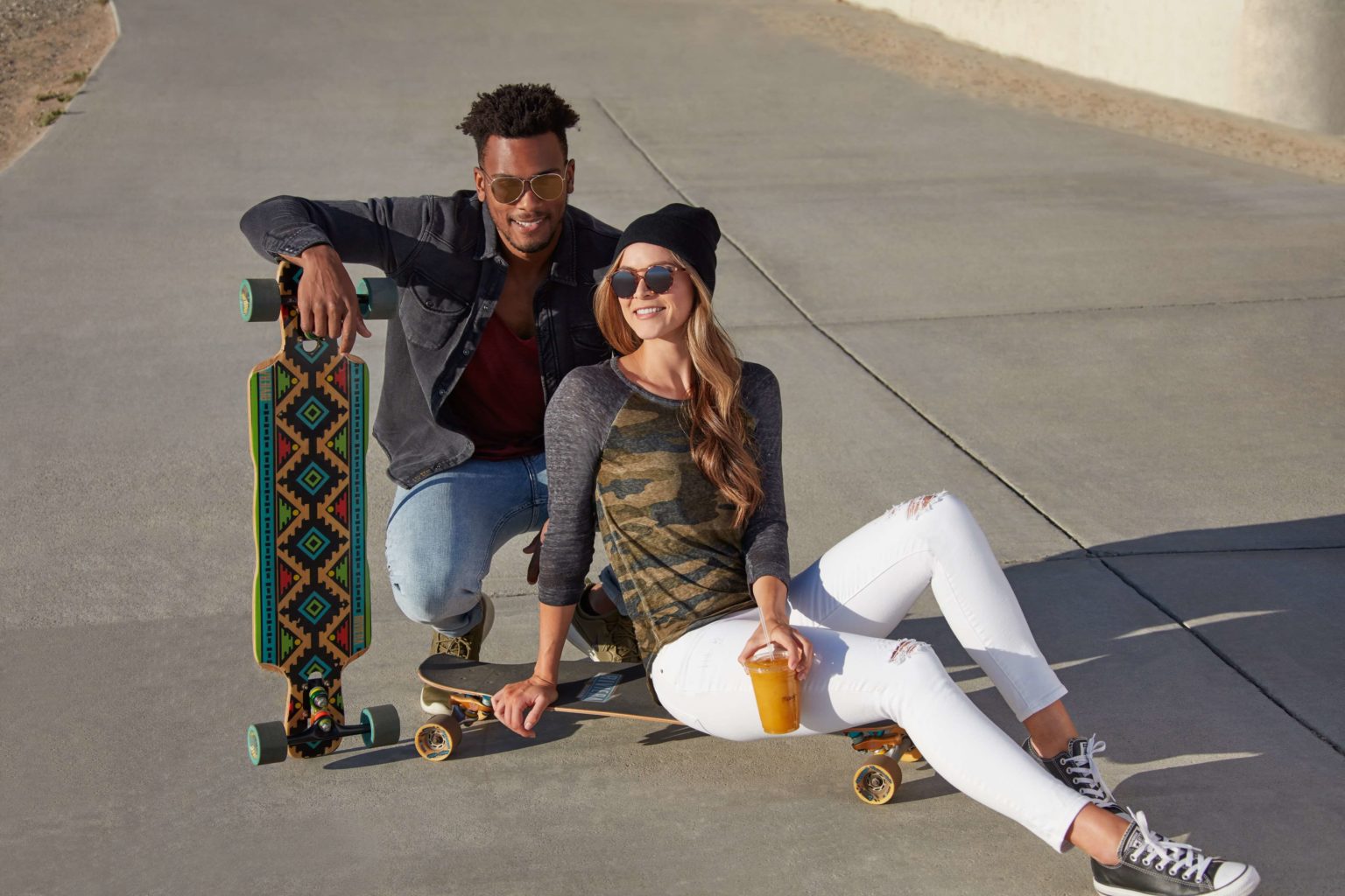 A guy and a girl with skate boards and a fruit juice in girl's hand given a phose for a look book