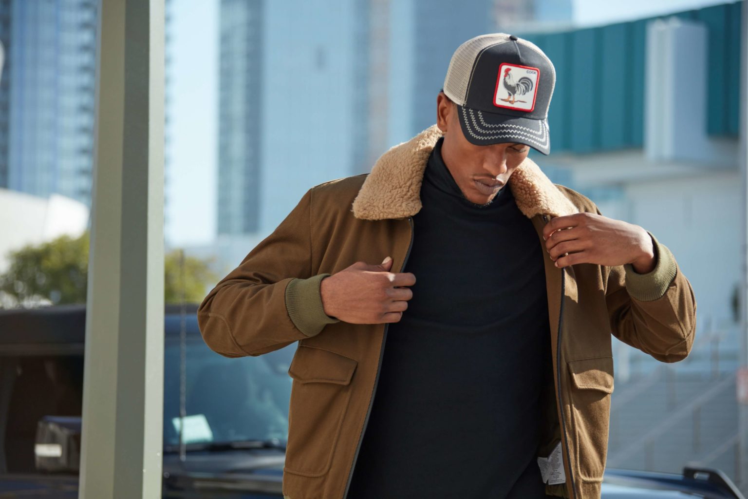 A male model walking on road wearing a tan color sweater and a cap