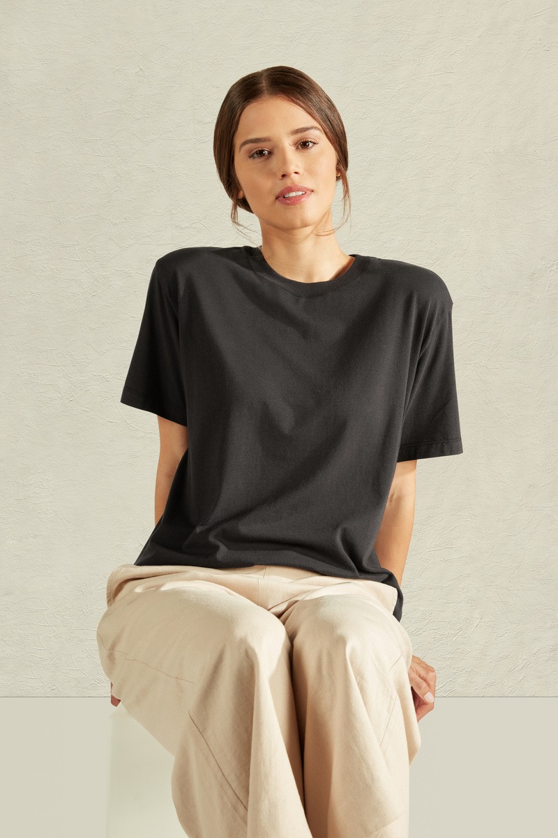 A female model wearing long cream pants and black tshirt sitting on a chair