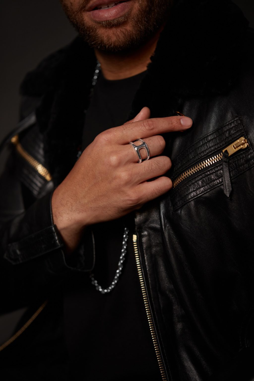 A male model with black jerkin showing his hand with a ring on his finger