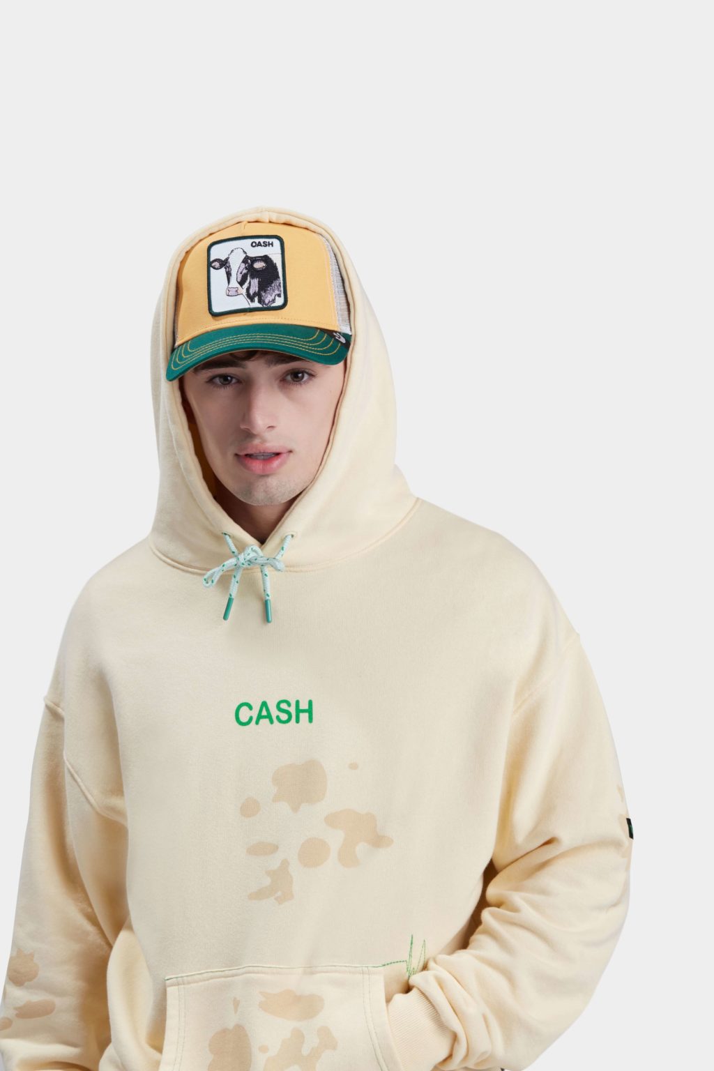 A young male model with cream color sweat shirt hoodie and a cap