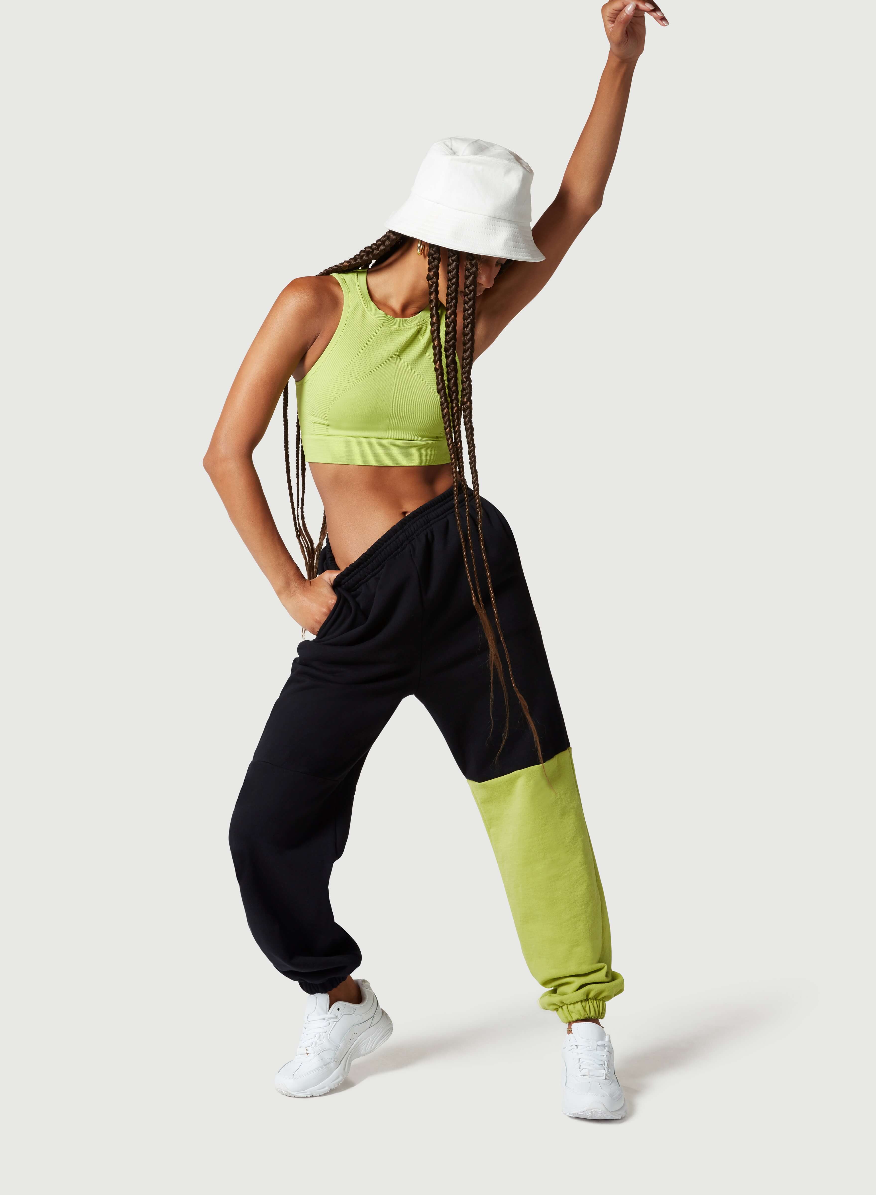A female model with black trousers, green top and white cap in a dancing position