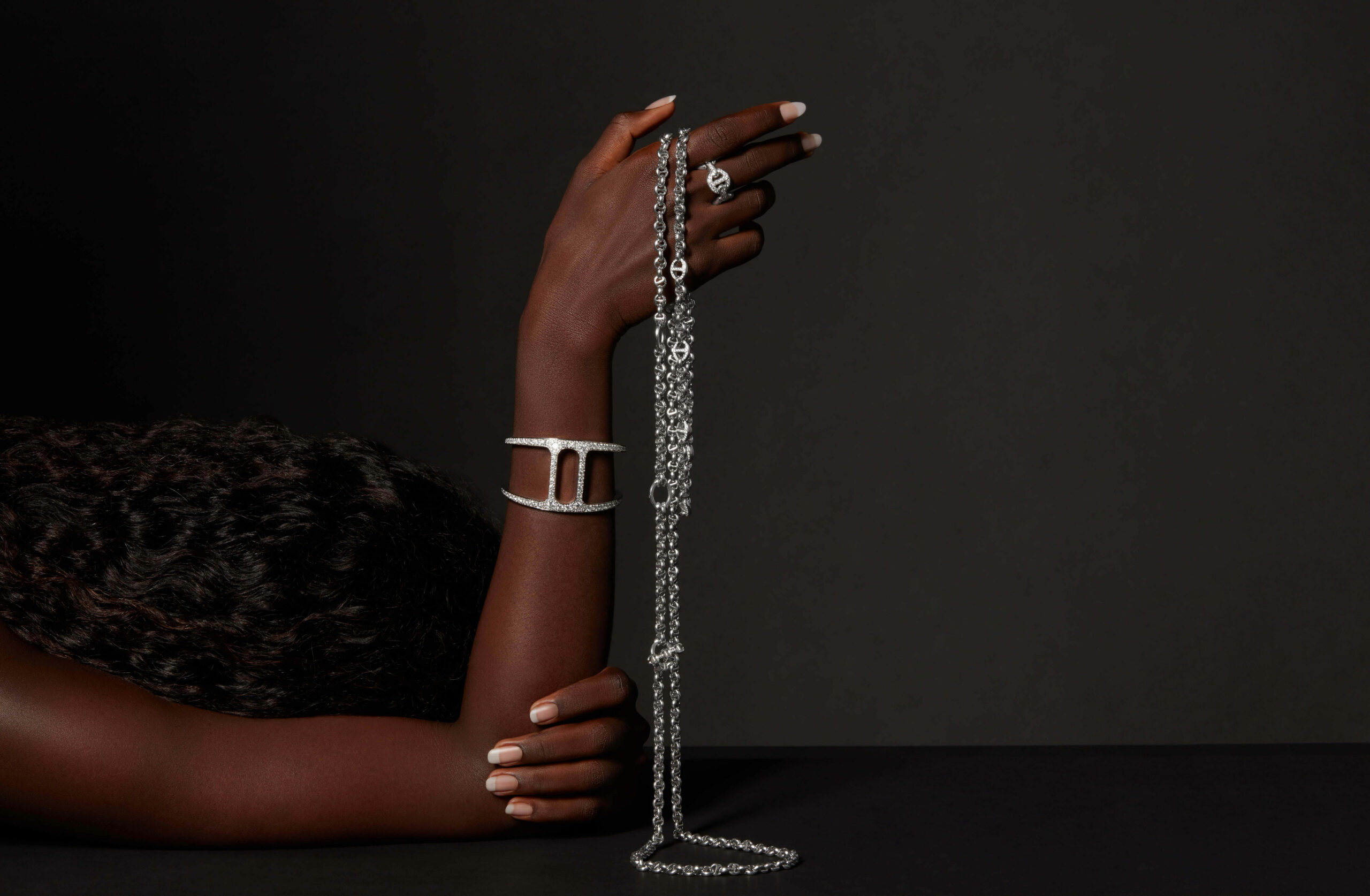 Image of a chain with ring and stylish hand cuff with diamonds holding by a woman hand