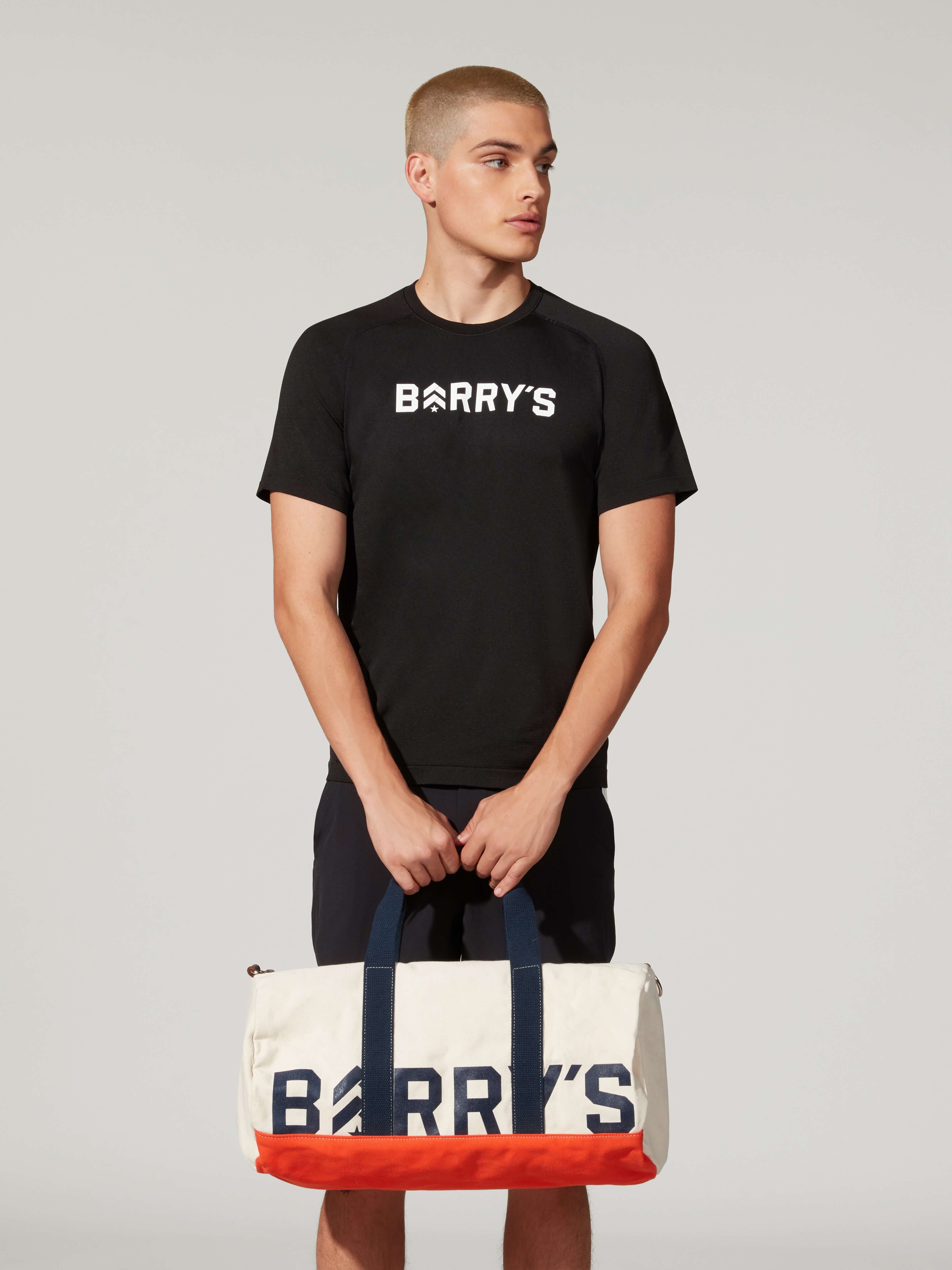 A male model with black Barry's tshirt , short and a Barry's bag