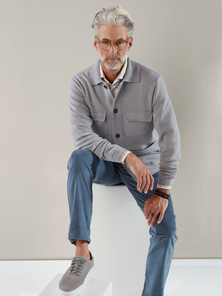 An old male model with formal dress, eye glasses and a over coat sitting on a chair