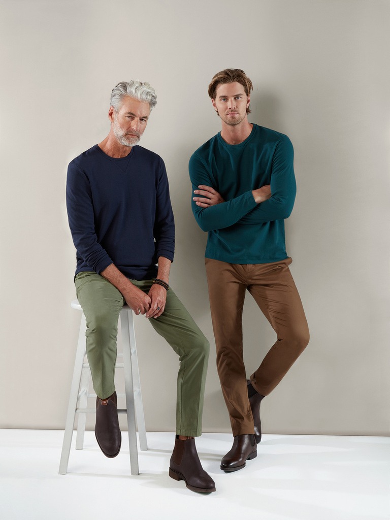 A sitting older male model and a standing younger male model in trousers and tshirts