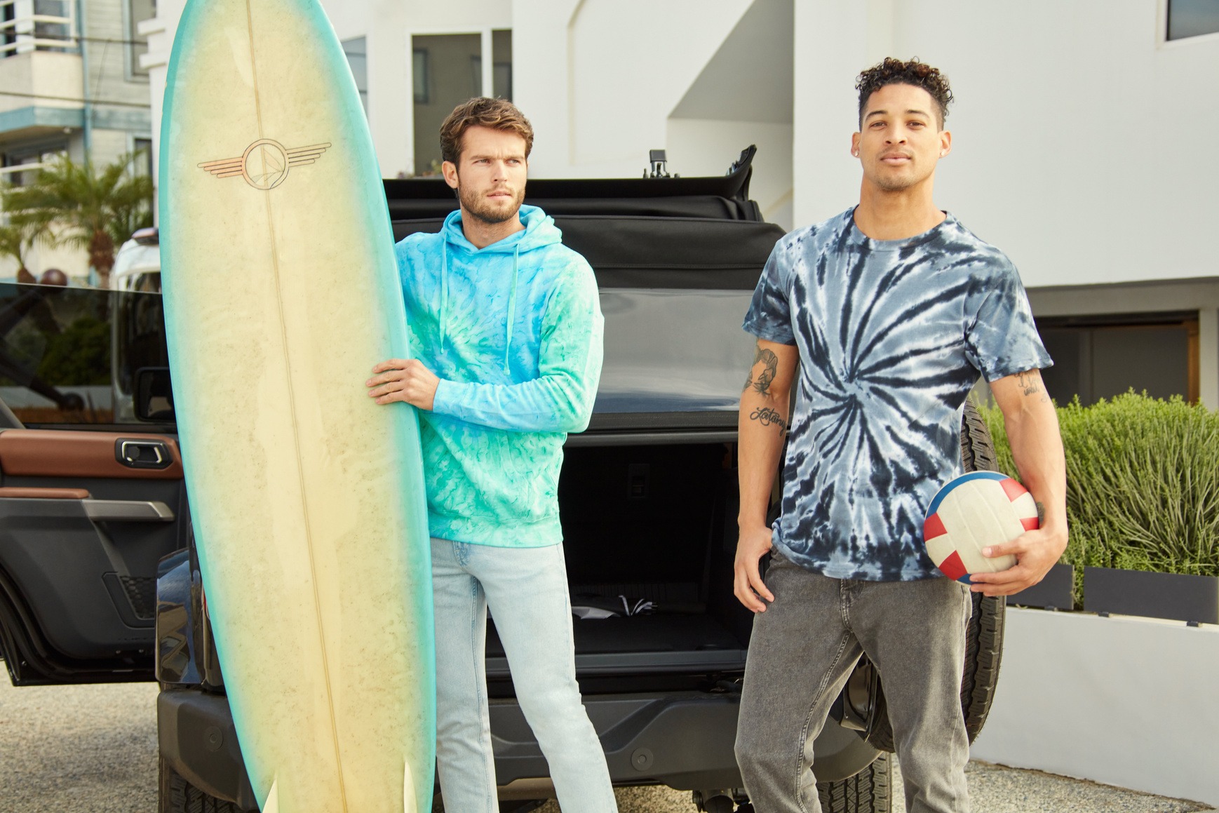 Two male models , one with water skiing board and another with a ball