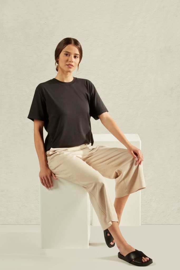 A female model wearing long cream pants and black tshirt sitting on a chair