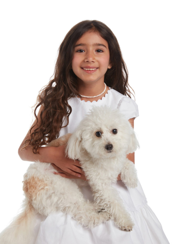 A cute little girl with white beads necklace and a puppy in her lap